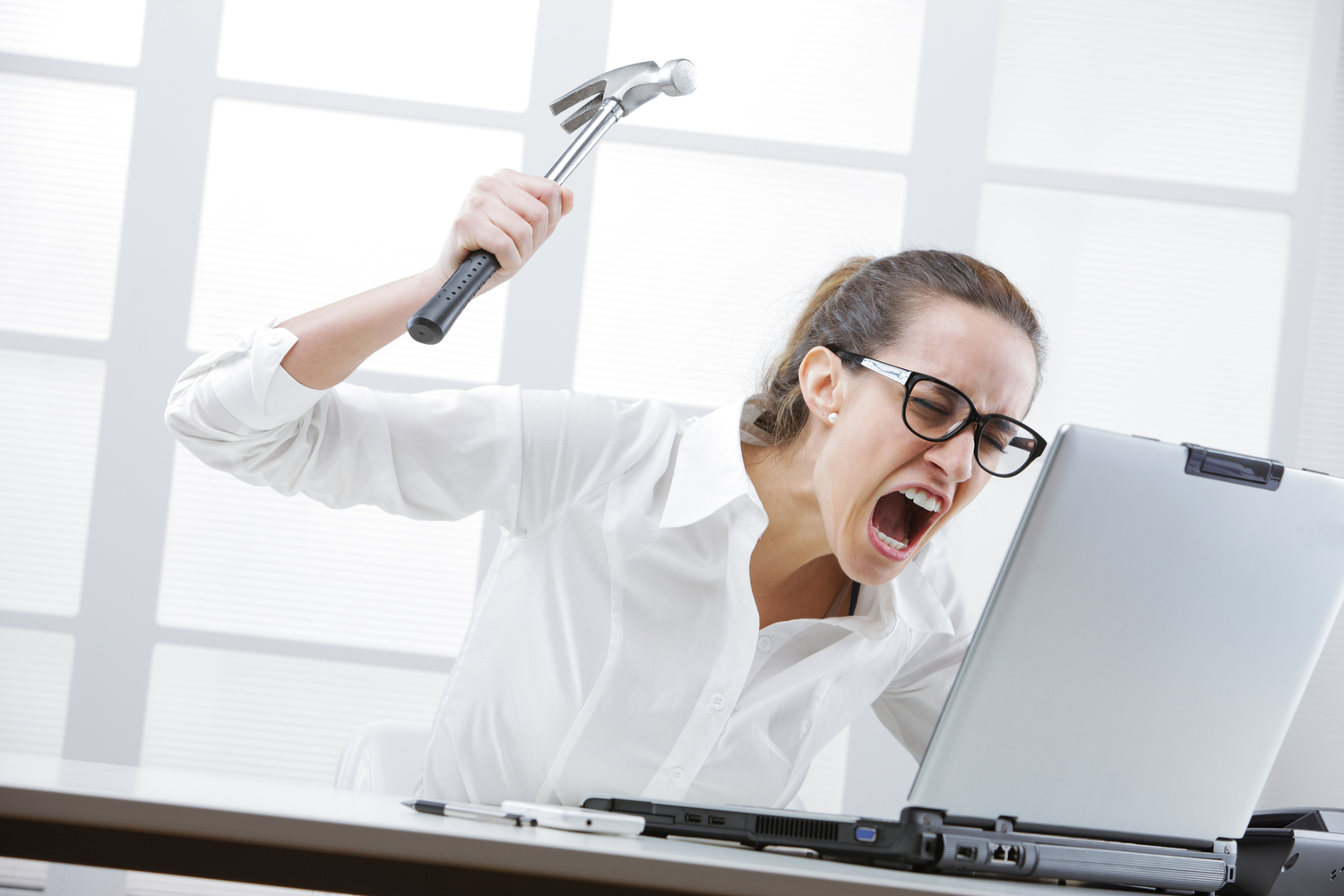 Freaked out businesswoman with a hammer ready to smash her laptop computer