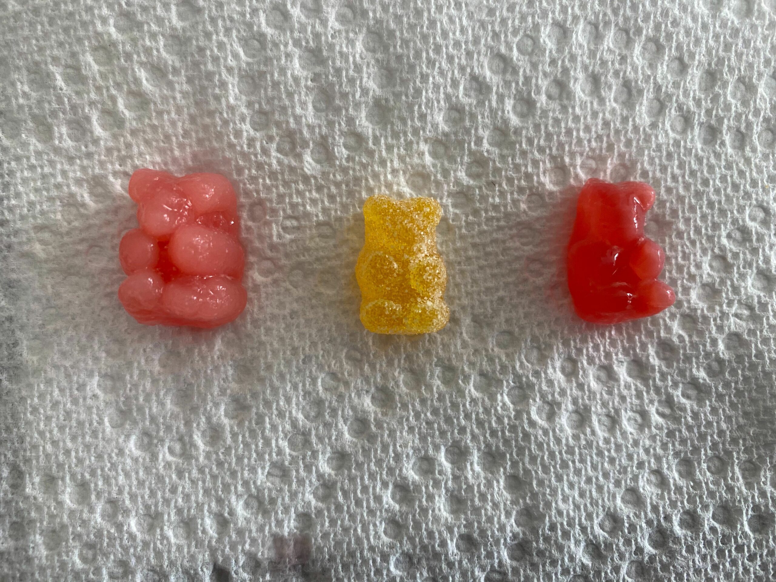 Close-up of three gummy bears (yellow and pink) on a textured white surface