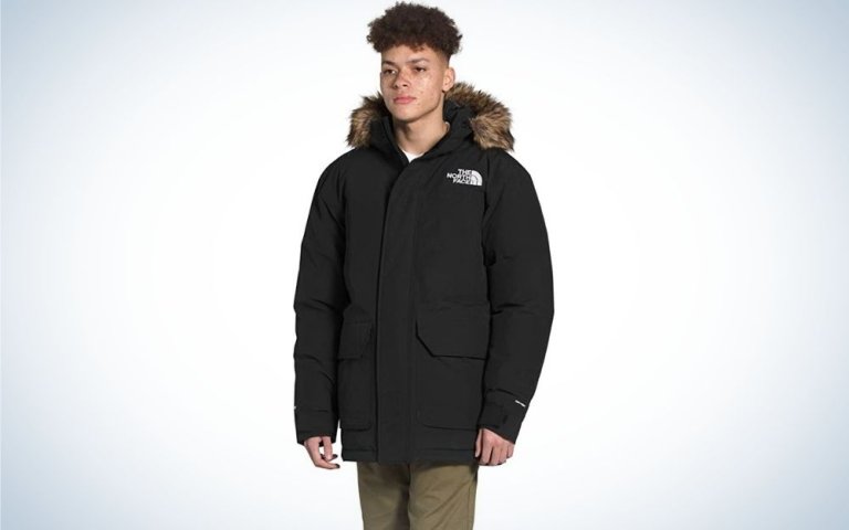 A young man wearing a big and warm winter jacket with black color and stuffed hood.