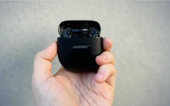 A person holding a pair Bose QuietComfort Ultimate against a plain wall.