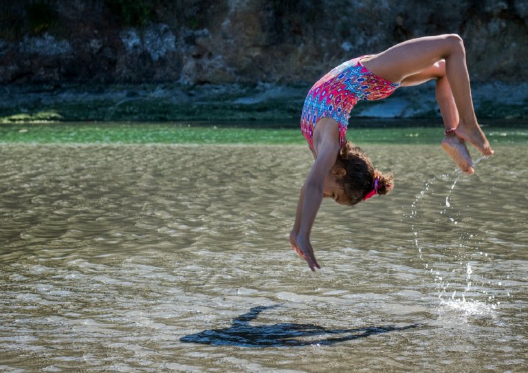 Kid in pink bathing suit doing a flip in a lake