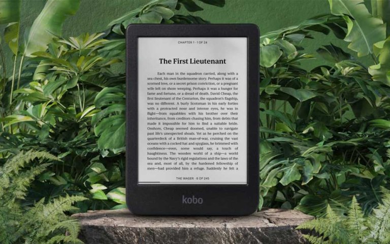 A Rakuten Kobo Clara BW ereader resting on a log surrounded by foliage