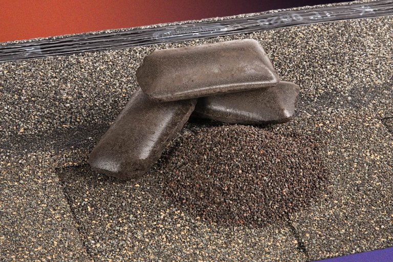 An asphalt shingle with some recycled shingle granules and packed asphalt briquettes on top of it, part of GAF's shingle recycling process.