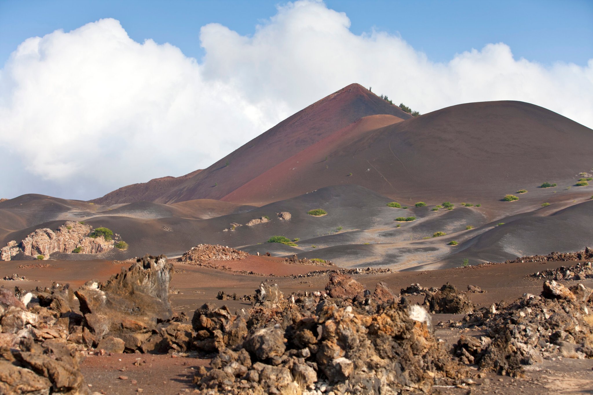 a reddish orange sharp peaked mountain formed from volcanic activity. the surrounding landscape is filled with dramatic orange and red rock