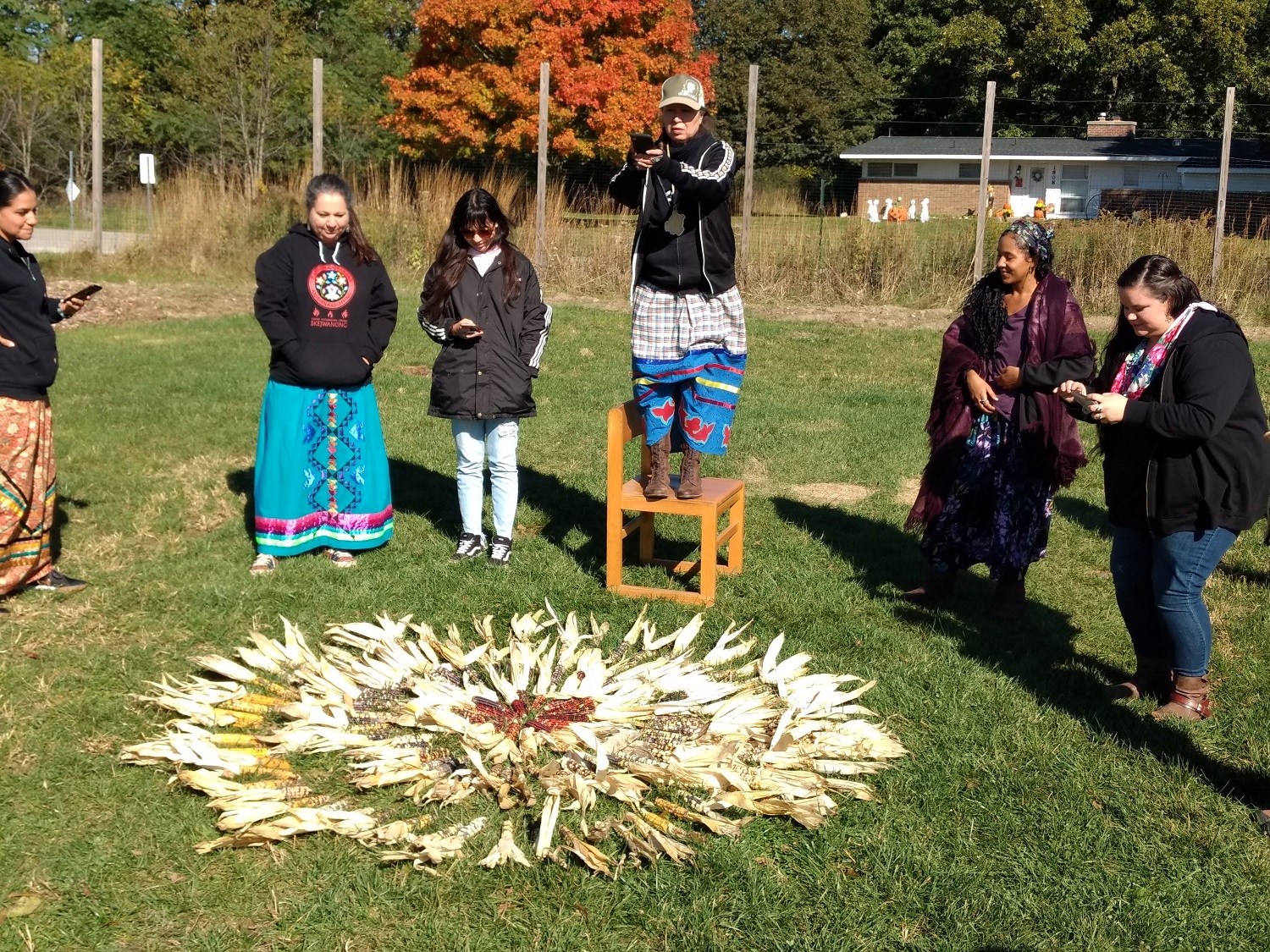 Tribal members in a circle around a ring of corn in the grass