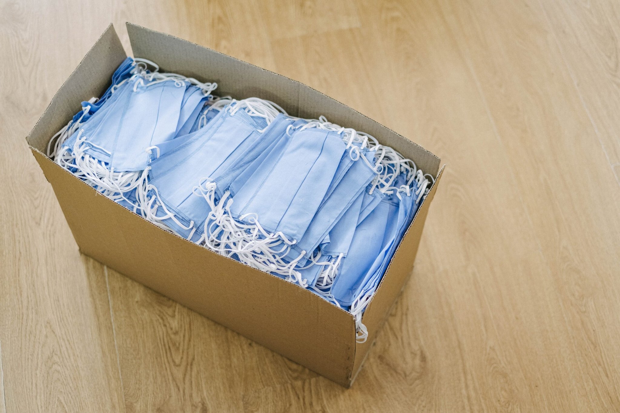Box of COVID-19 medical masks on wooden floor.