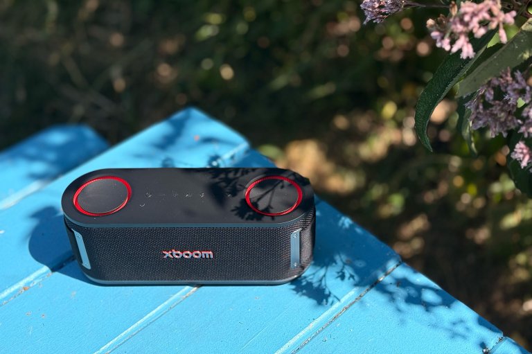 An LG xboom Bounce speaker on a blue picnic table with flowers in the background