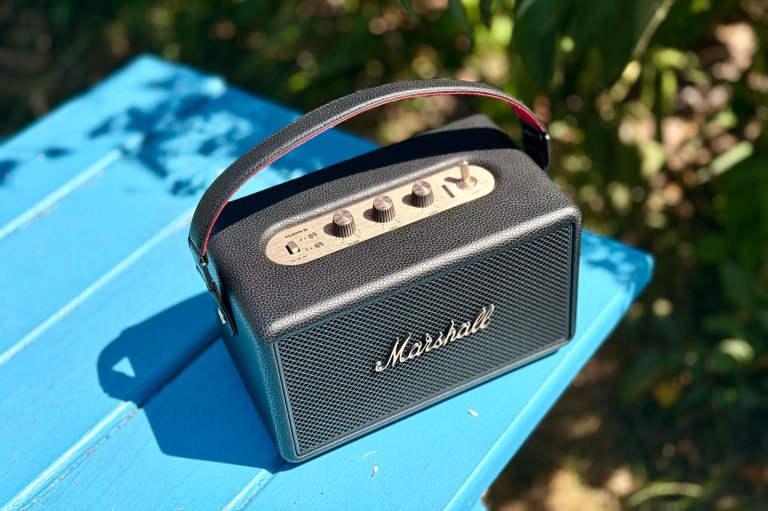 A black and gold Marshall Kilburn III portable speaker sitting on a blue picnic table