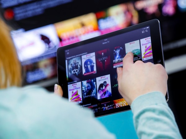 Woman Holding a touch pad and switching channels on France Netflix HomePage. with TV set on background