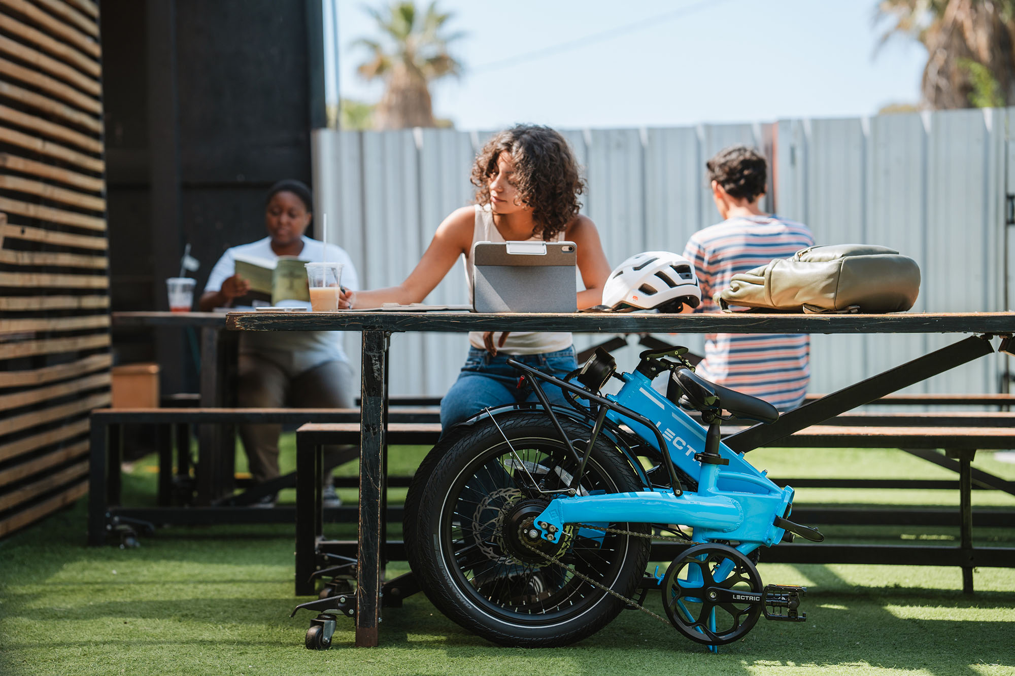 A blue XP Lite 2.0 folding bike folded in front of a woman at a picnic table
