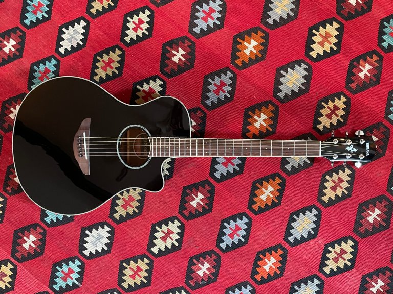 A black Yamaha APX6000 electric-acoustic guitar flat on a colorful red Southwestern rug