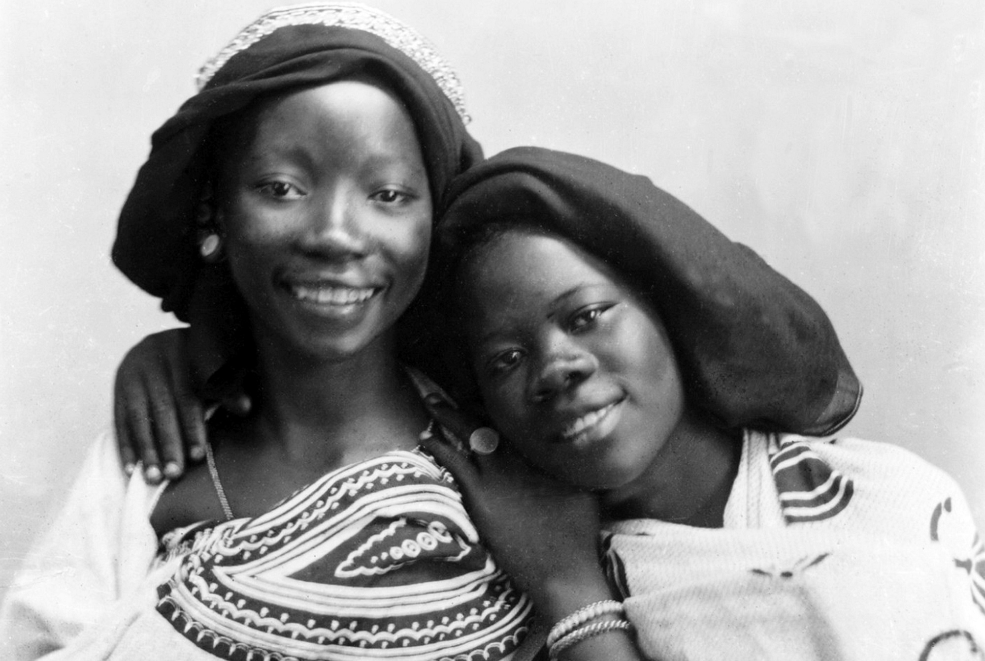 Two Swahili women in traditional headwear and dresses. Black and white portrait.