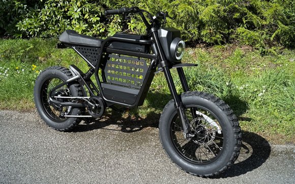 A black Ride1Up Revv DRT moto-style e-bike in a driveway in front of green green grass