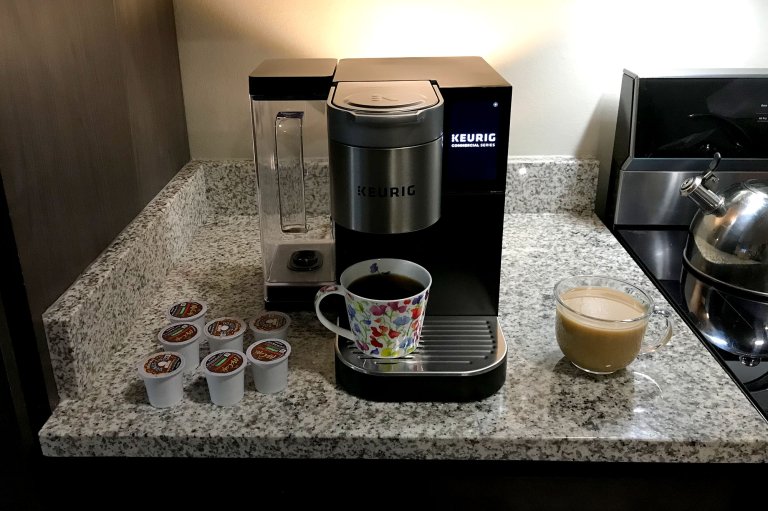 A Keurig Medium Commercial Series coffee maker on a countertop with a selection of K-Pods and a cup of warm coffee