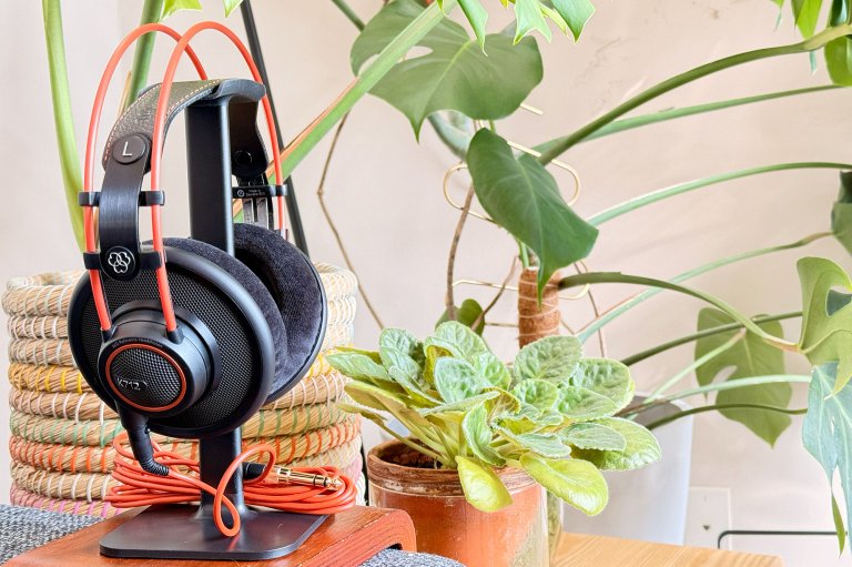 AKG K712 Pro black-and-orange headphones on a stand in front of a bunch of bright green plants