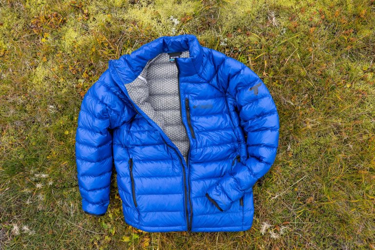 Blue Columbia Sportswear Arctic Crest puffer laying on green lichen in Iceland, its Omni-Heat Arctic lining exposed