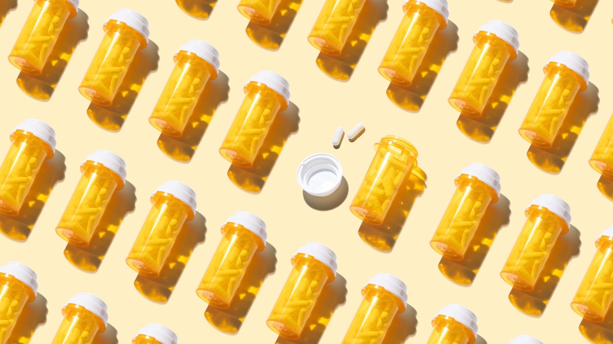 An Opened Prescription Medicine Bottle Among Many Other Sealed Bottles on Yellow Background High Angle View.