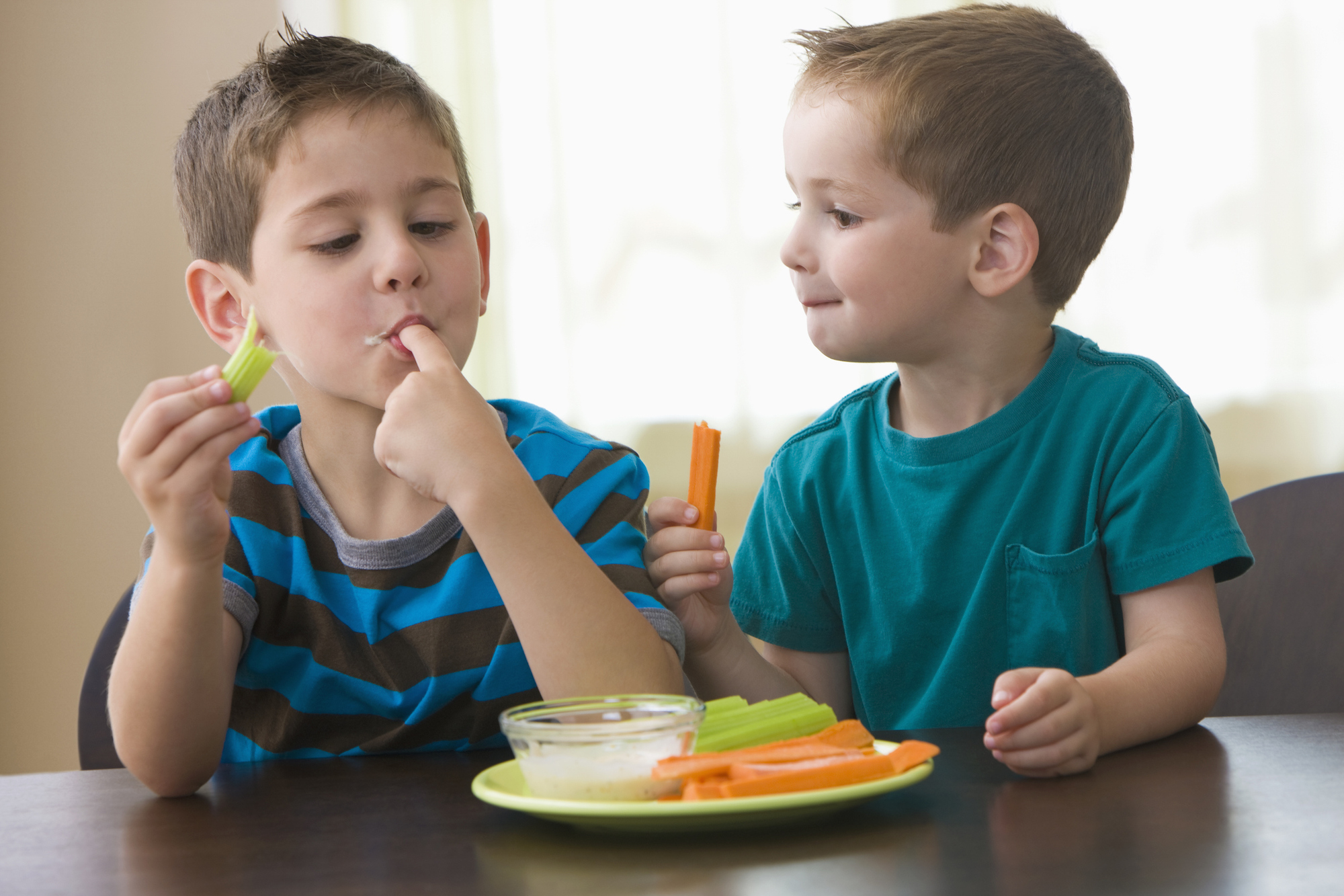 two kids eating carrots and celery with a ranch dressing dip
