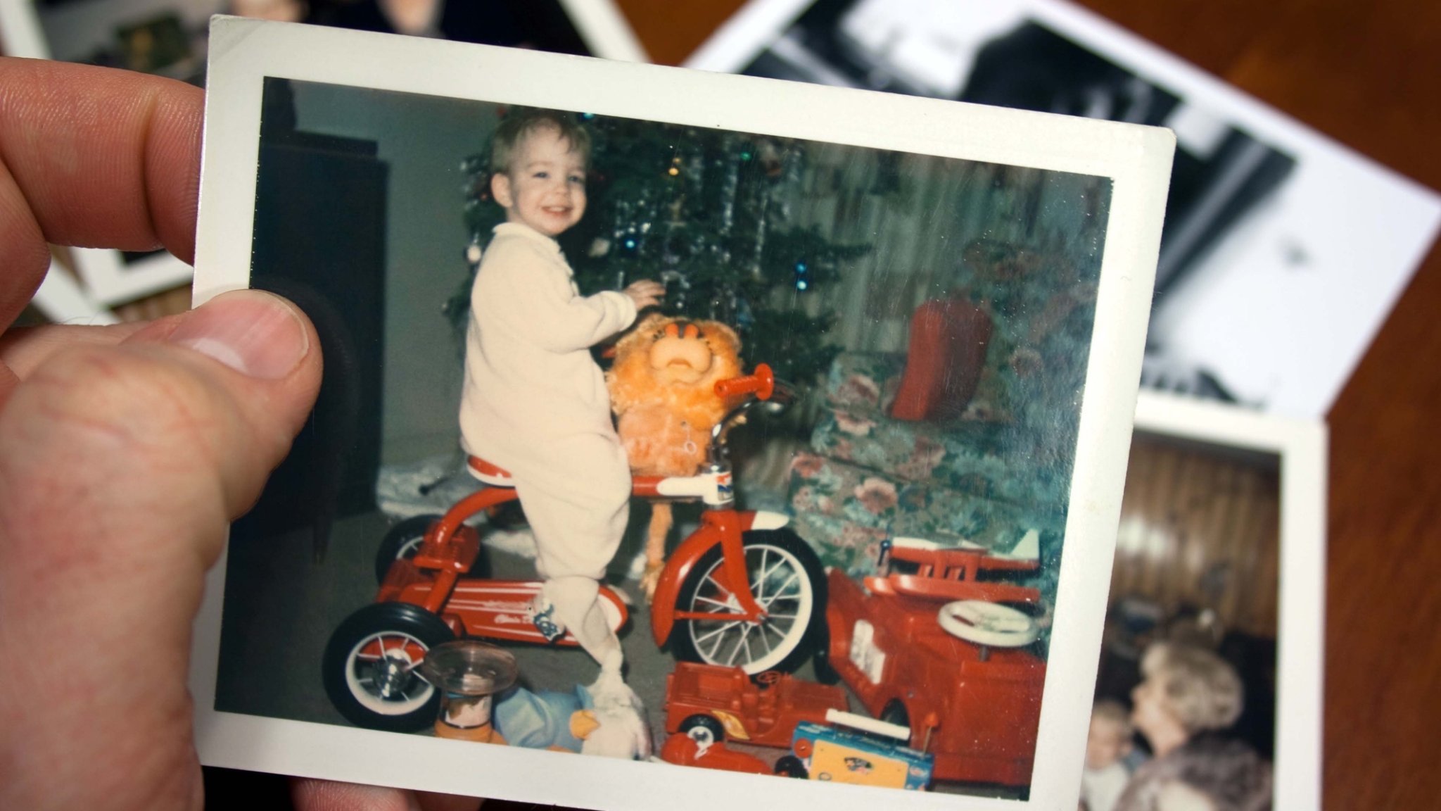 Hand holds Vintage photograph of boy on tricycle at christmas