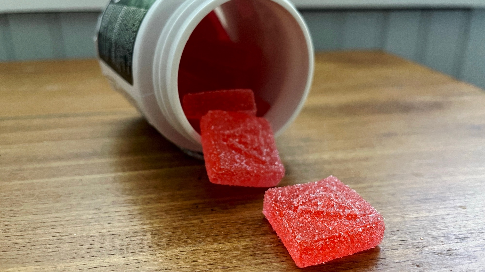 Cannabis Edible Gummies spilling from container onto wood table