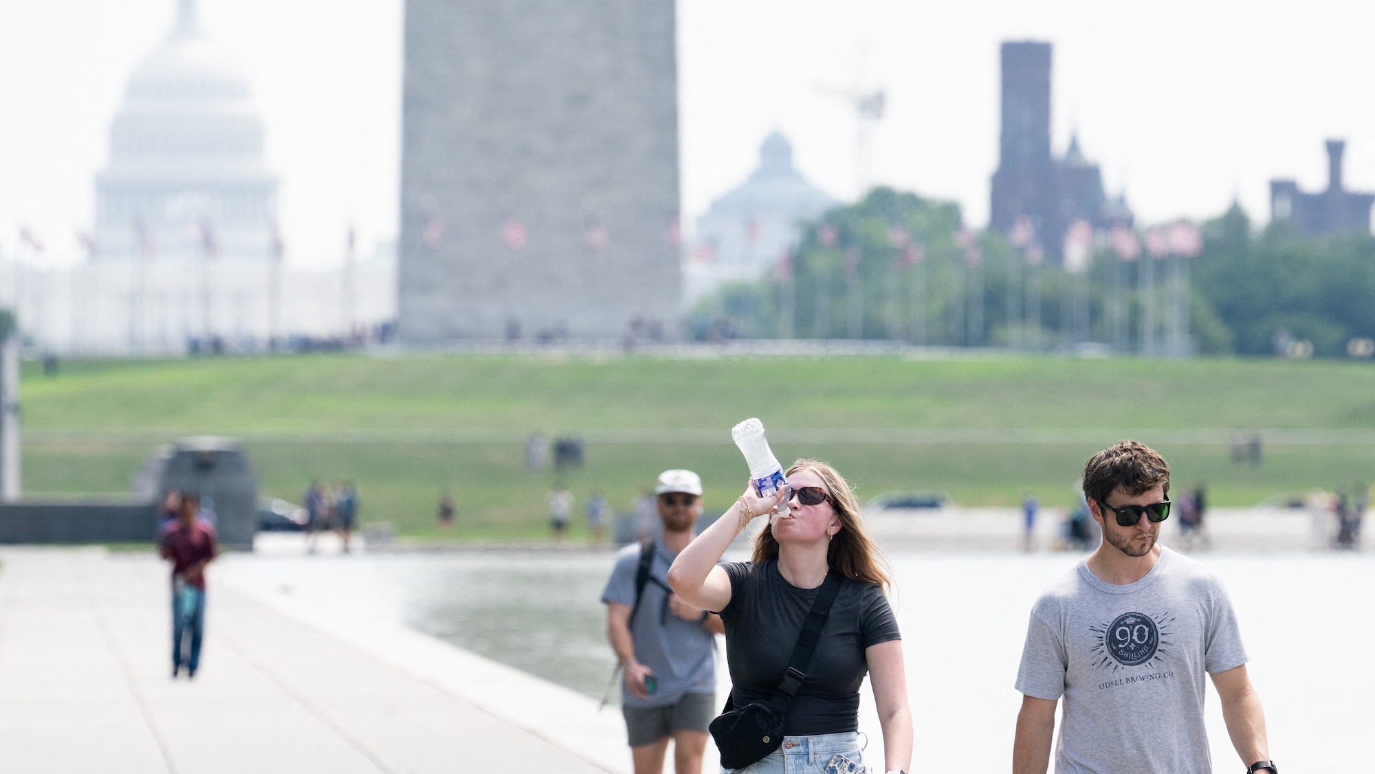 Tourists drink water as they walk along the National Mall near the Washington Monument in Washington, DC, July 25, 2025, as a heat dome sits over the region leading to extremely high temperatures. (Photo by SAUL LOEB / AFP)