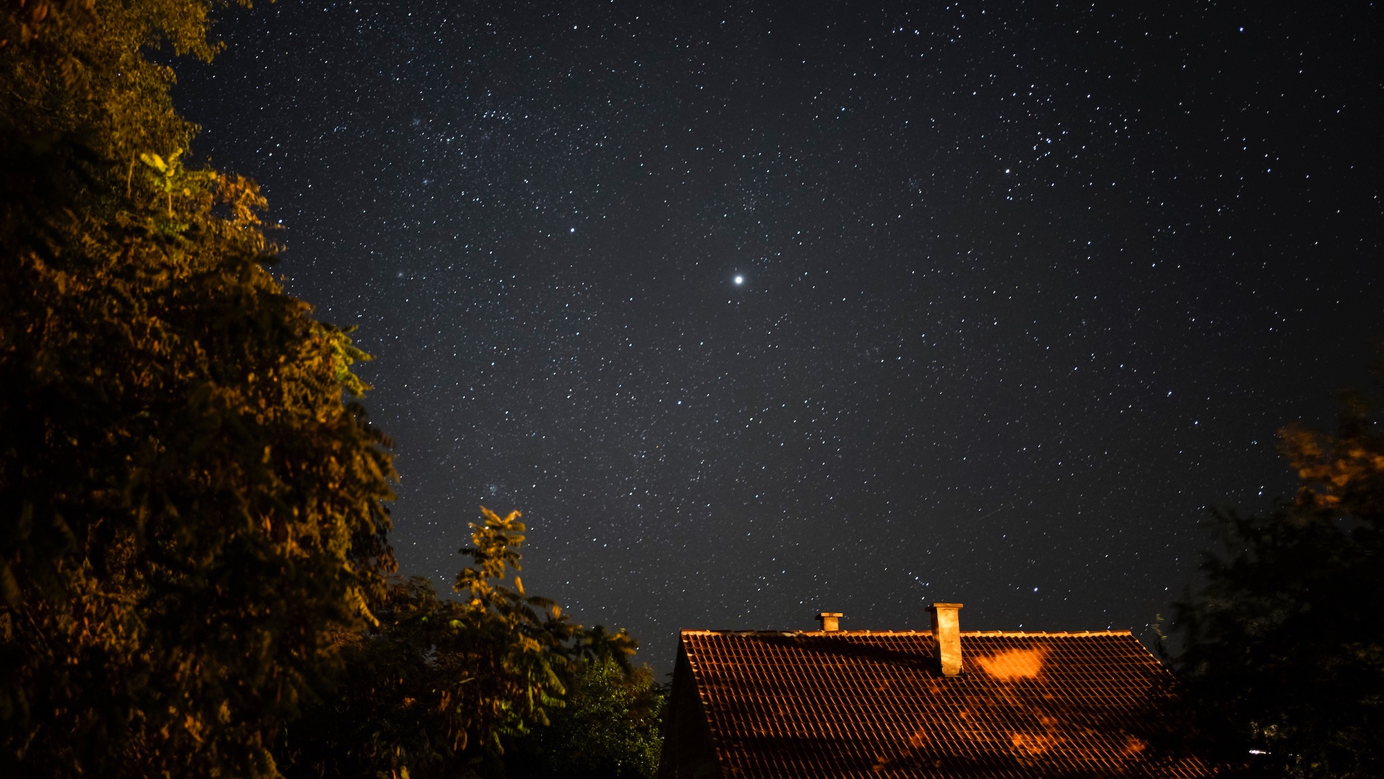Star - Space with the Pleiades over the roof of a residential house.