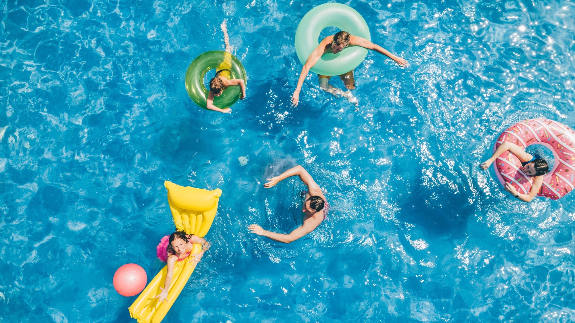 Friends having fun while playing with ball in the swimming pool. Aerial view.