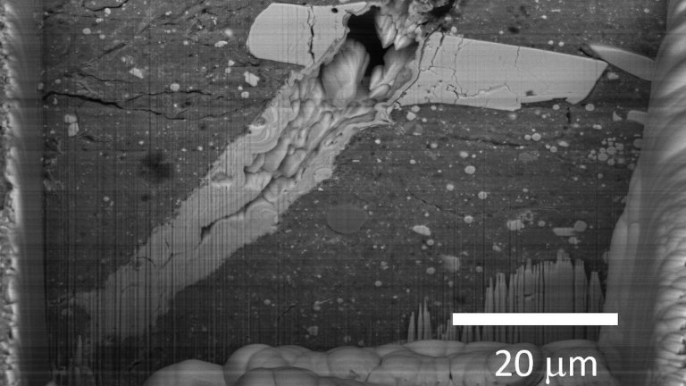 A scanning electron microscope image of a micrometeorite impact crater in a particle of asteroid Bennu material.
