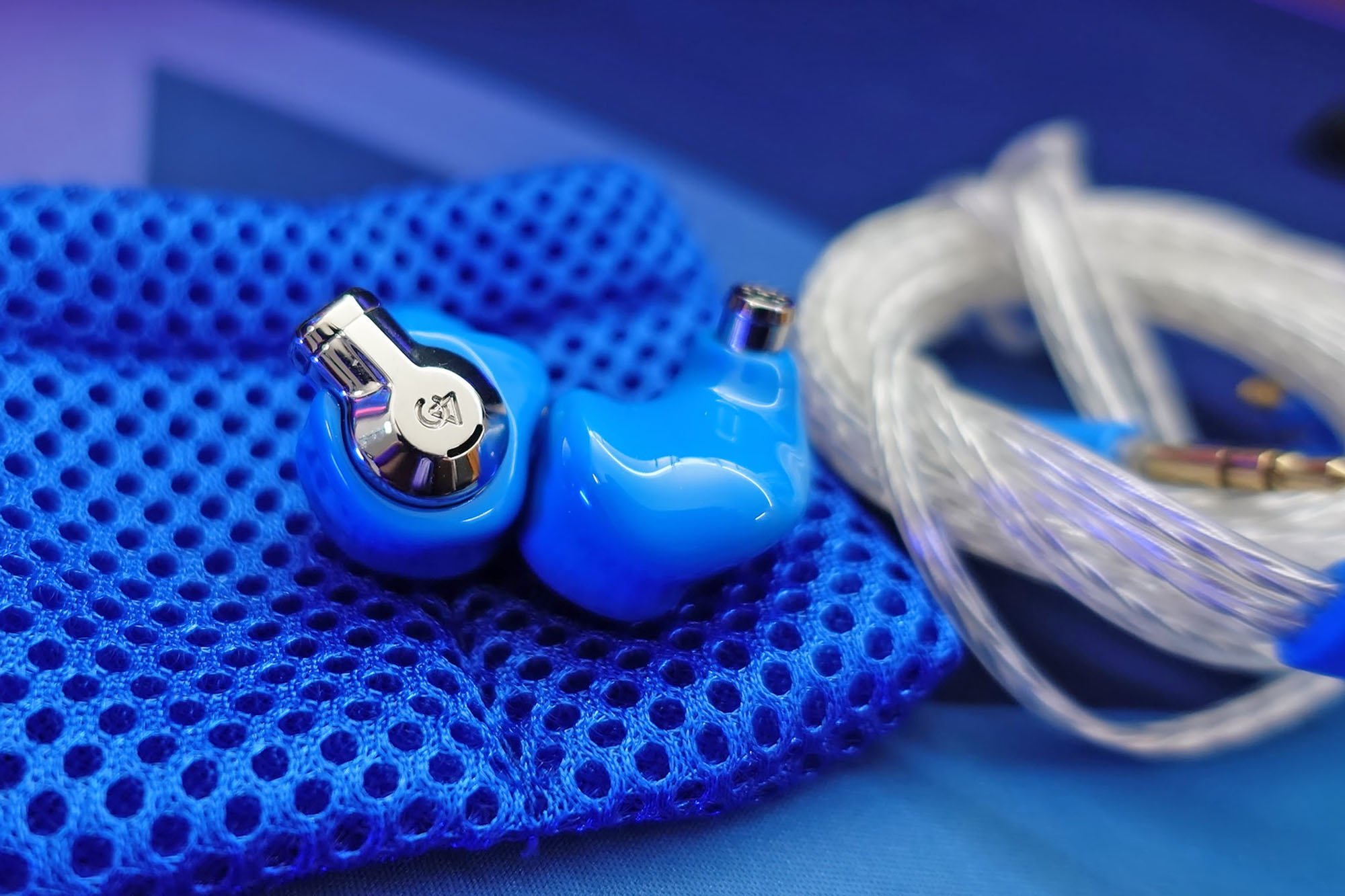 Very blue Campfire Audio Cascara IEM on an even bluer mesh bag next to a silver cable
