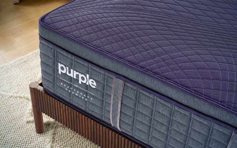 Close up of a corner of the Purple RejuvenatePremier mattress on a wooden bed frame