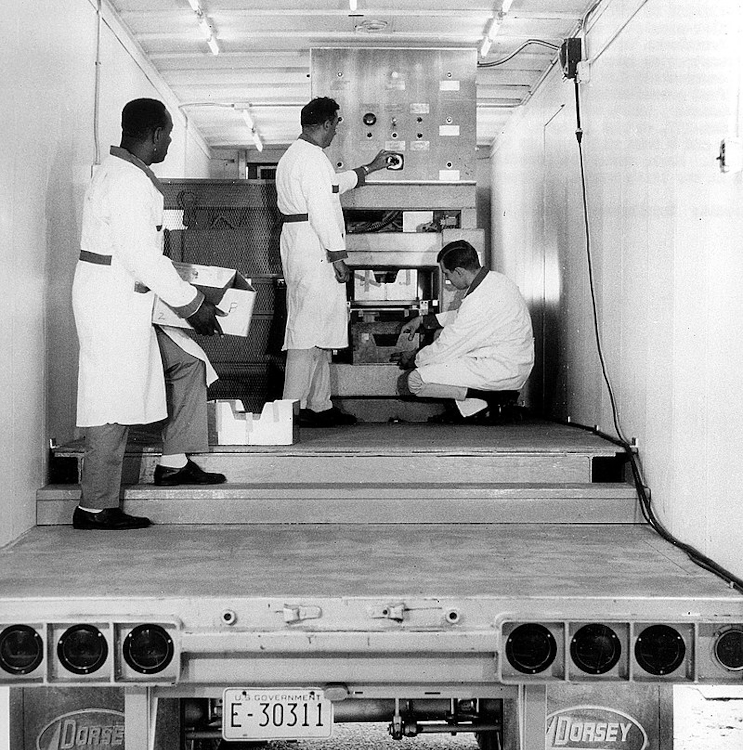 Three scientists working on a food irradiation machine inside a truck cargo compartment