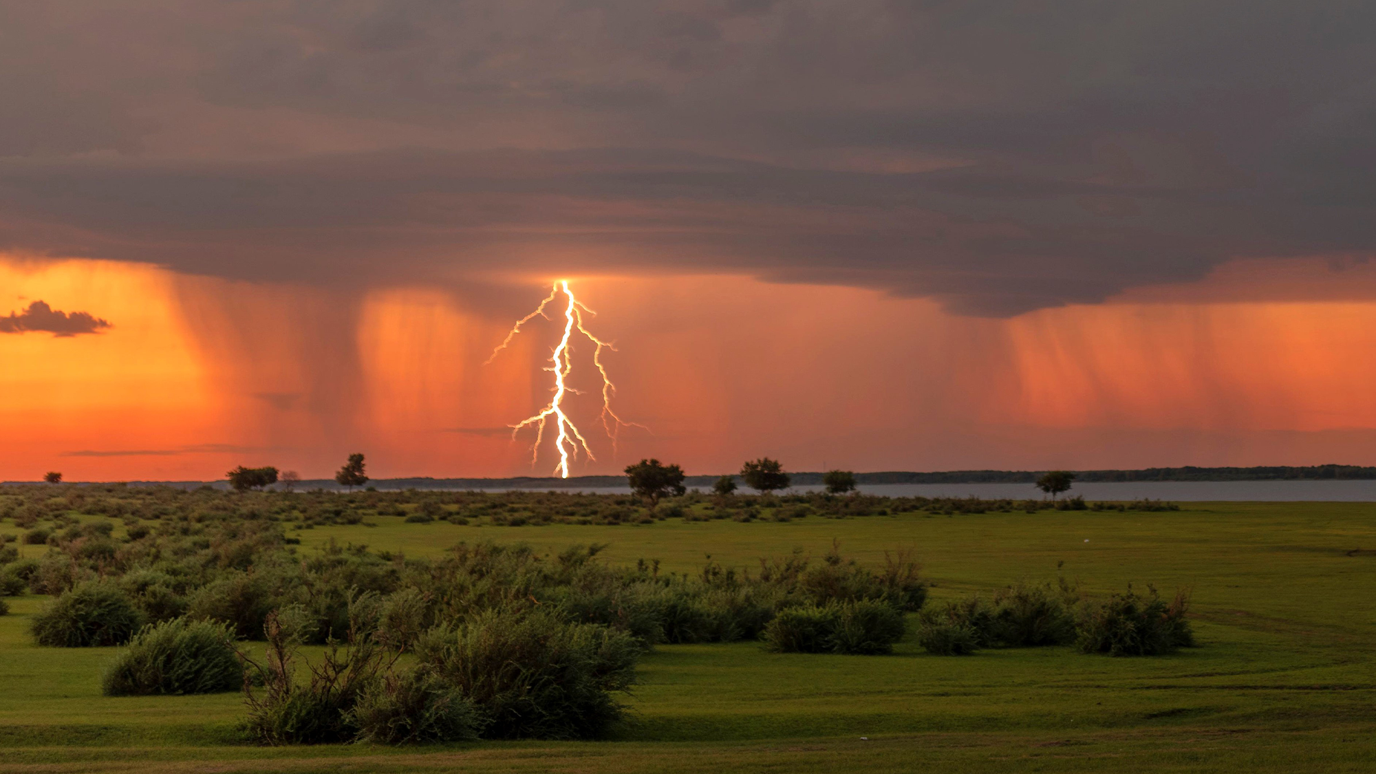 a stream of lightning touches the ground with sunlight in the background