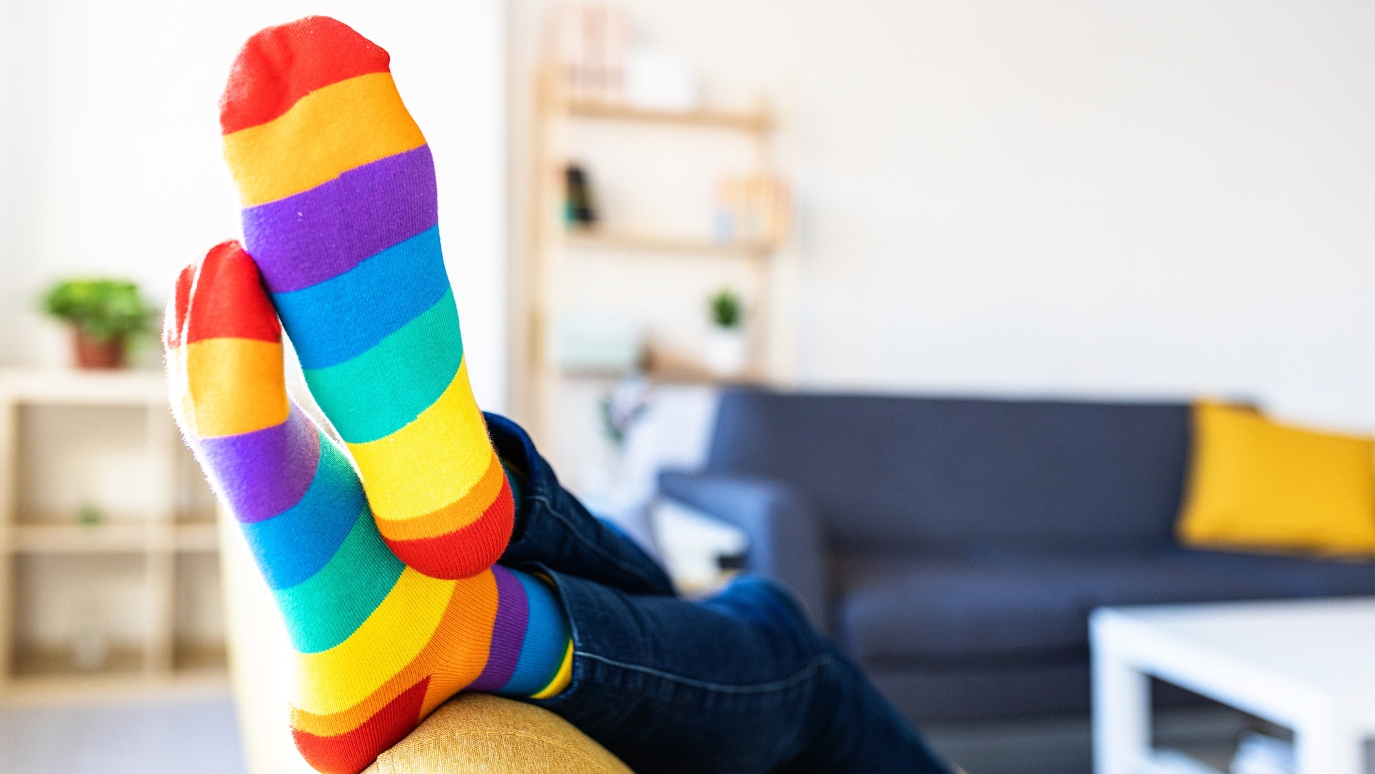 Close up view of a woman wearing colorful striped socks while relaxing on a sofa at home.