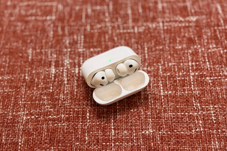 White AirPods Pro 3 earbuds in their case sitting open on red brick colored upholstery