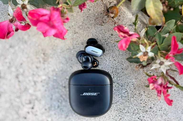 Bose QC Ultra Gen. 2 earbuds sitting on grey concrete under some pink flowers