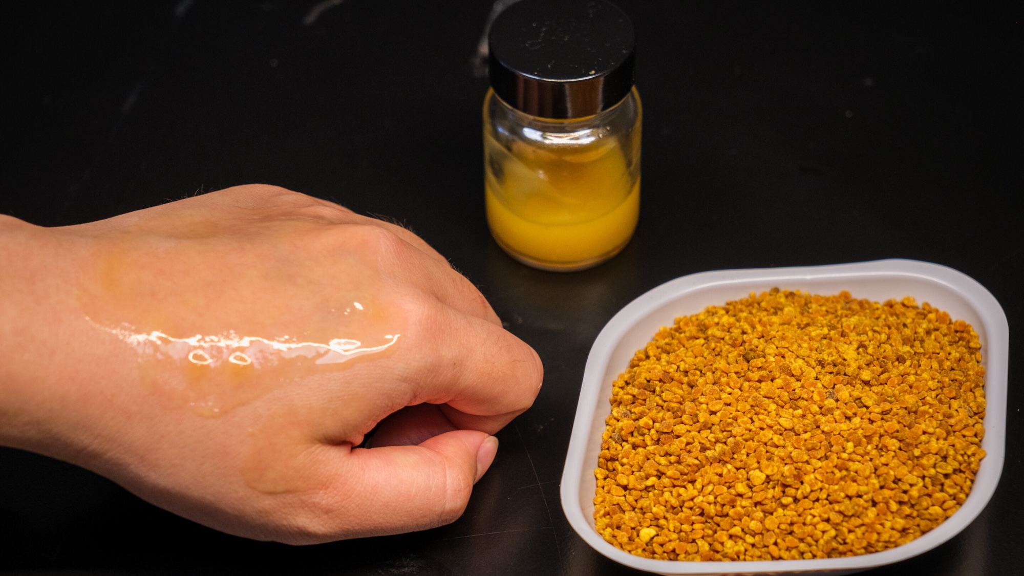 Mano con protector solar en microgel aplicado junto a un frasco de protector solar y un tazón de semillas de camelia utilizadas en la receta