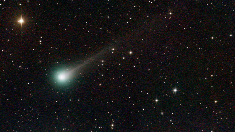 a comet with a green-ish tail streaking through a starry sky