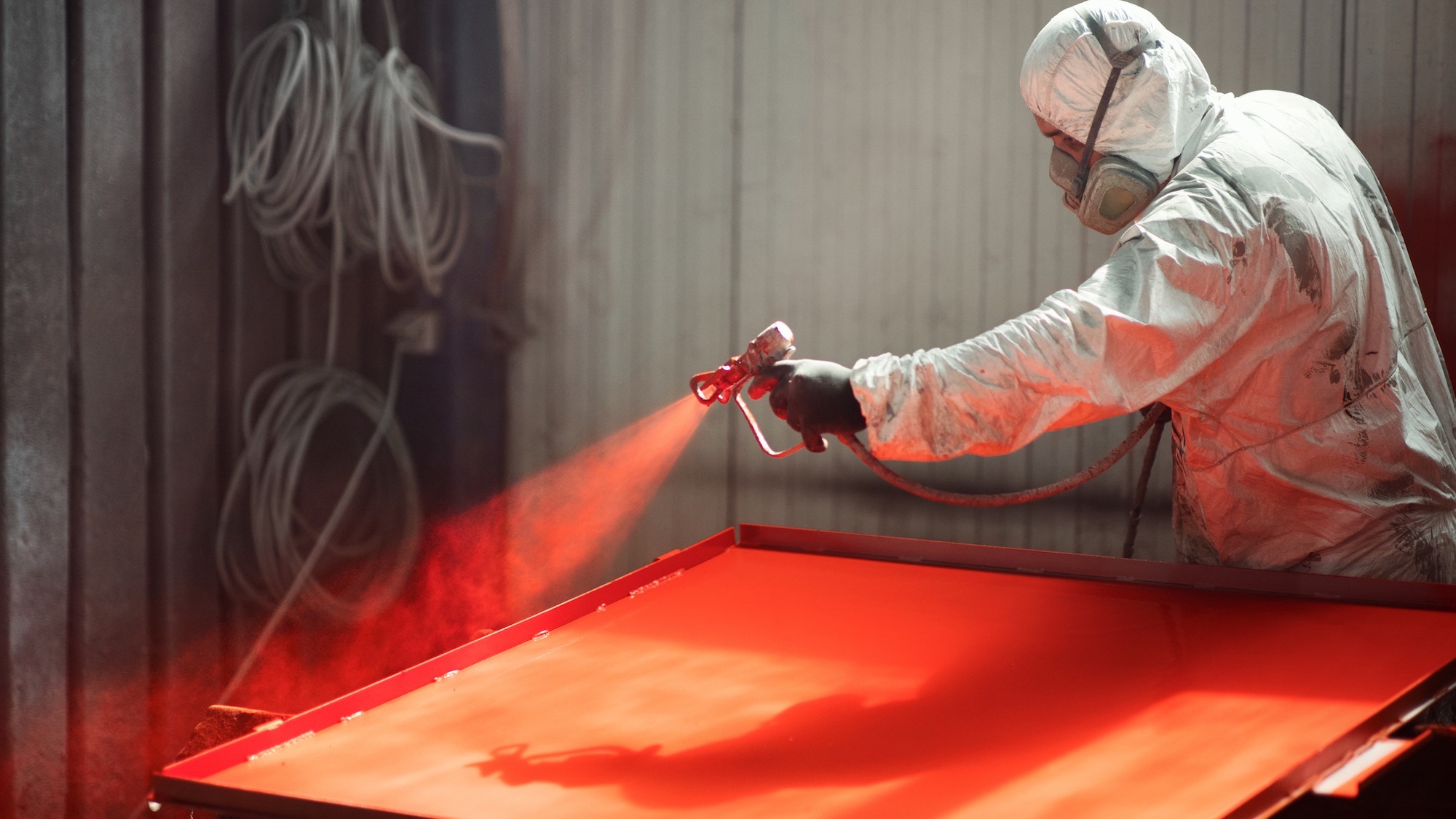 Closeup of an early 30's male using a compressor for spray painting steel plates at a factory facility.