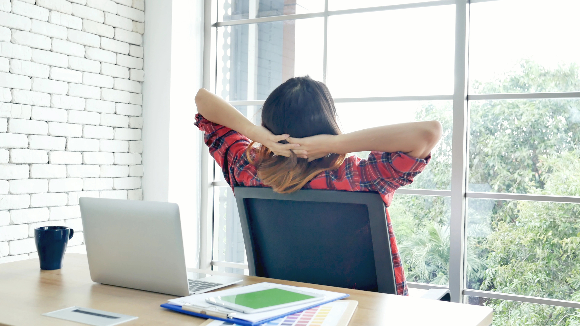 Woman leaning back in office chair at desk looking out window