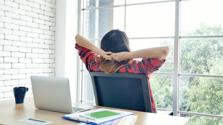 Woman leaning back in office chair at desk looking out window