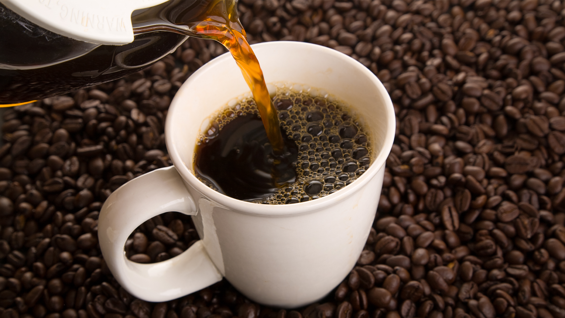 pouring coffee into a white cup that is sitting on coffee beans
