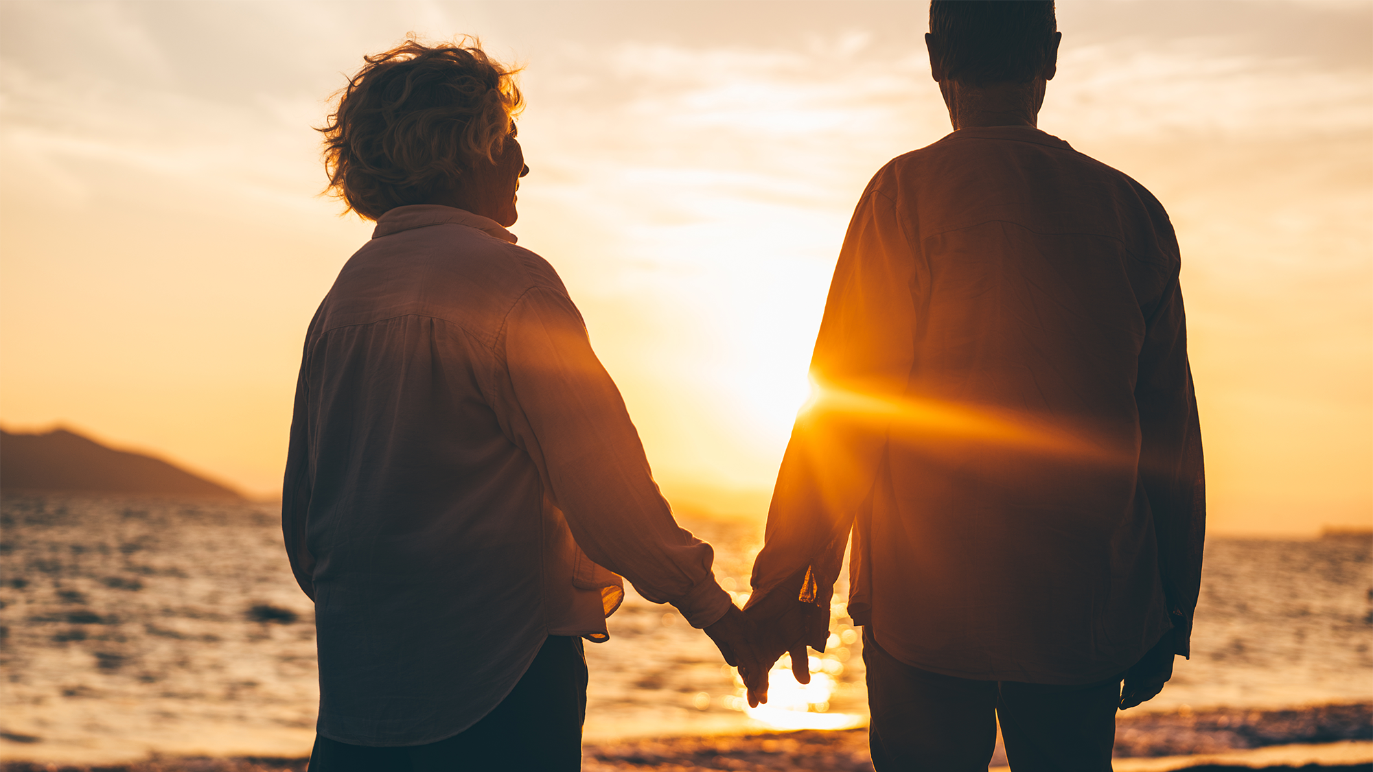 an older couple holding hands as the sun sets