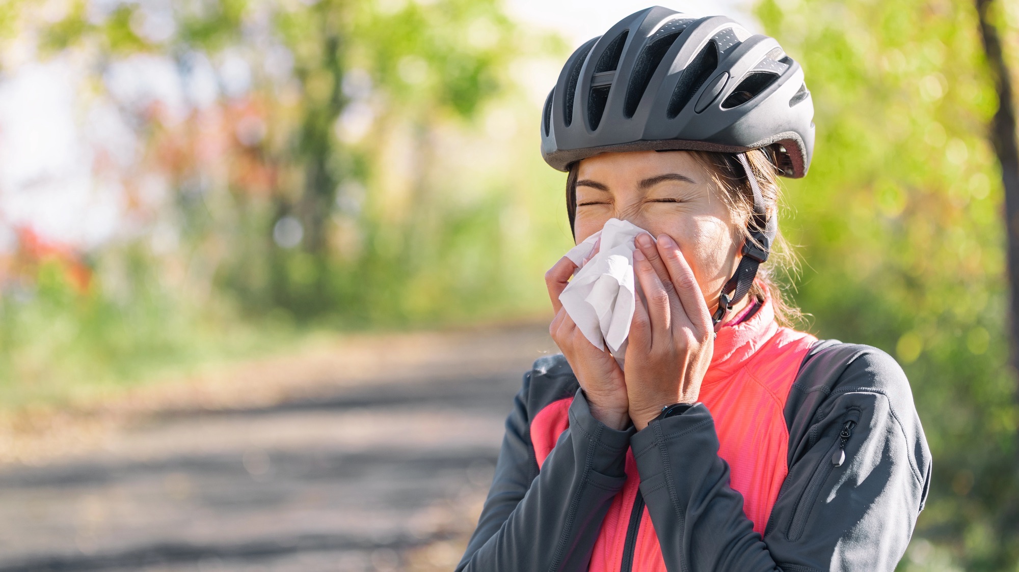 Cough in tissue covering nose and mouth when coughing outside as COVID-19 hygiene guidelines for Coronavirus spread prevention. Biking cyclist girl sneezing in paper outside.
