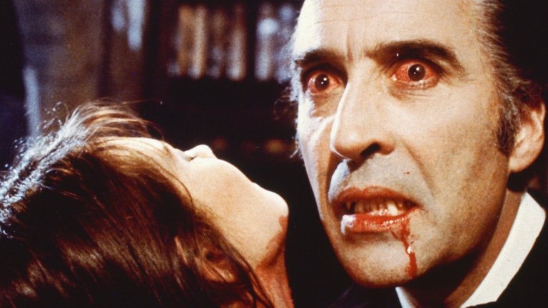 A close-up film still showing the face of an actor portraying Dracula, with bloodshot red eyes, blood dripping from his mouth, and pointed fangs visible. To the left, a woman's pale neck and chin, stained with blood, are visible as she is held by the vampire. The lighting is dark and dramatic.