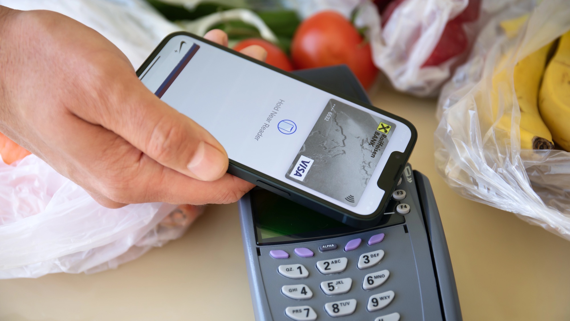 Man hand holding Apple iPhone 13 with Apple Pay on the screen and POS pay pass online terminal.