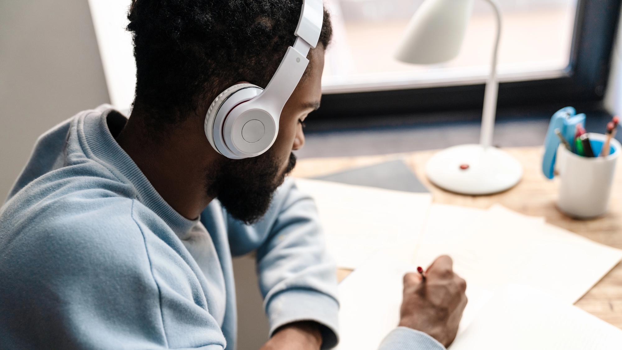 Man listening to headphones while writing at desk