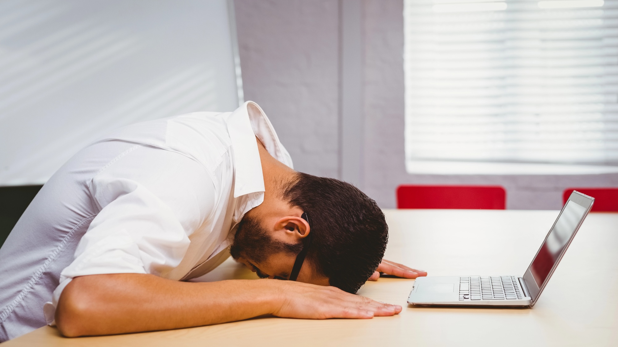 Man with his head down on his desk in front of laptop from stress