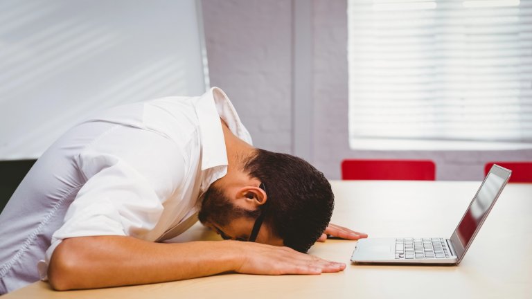 Man with his head down on his desk in front of laptop from stress