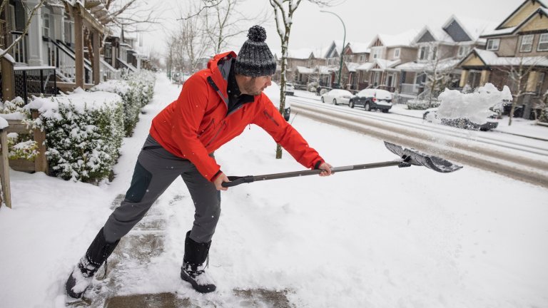 Man shoveling snow off his sidewalk after a winter storm.