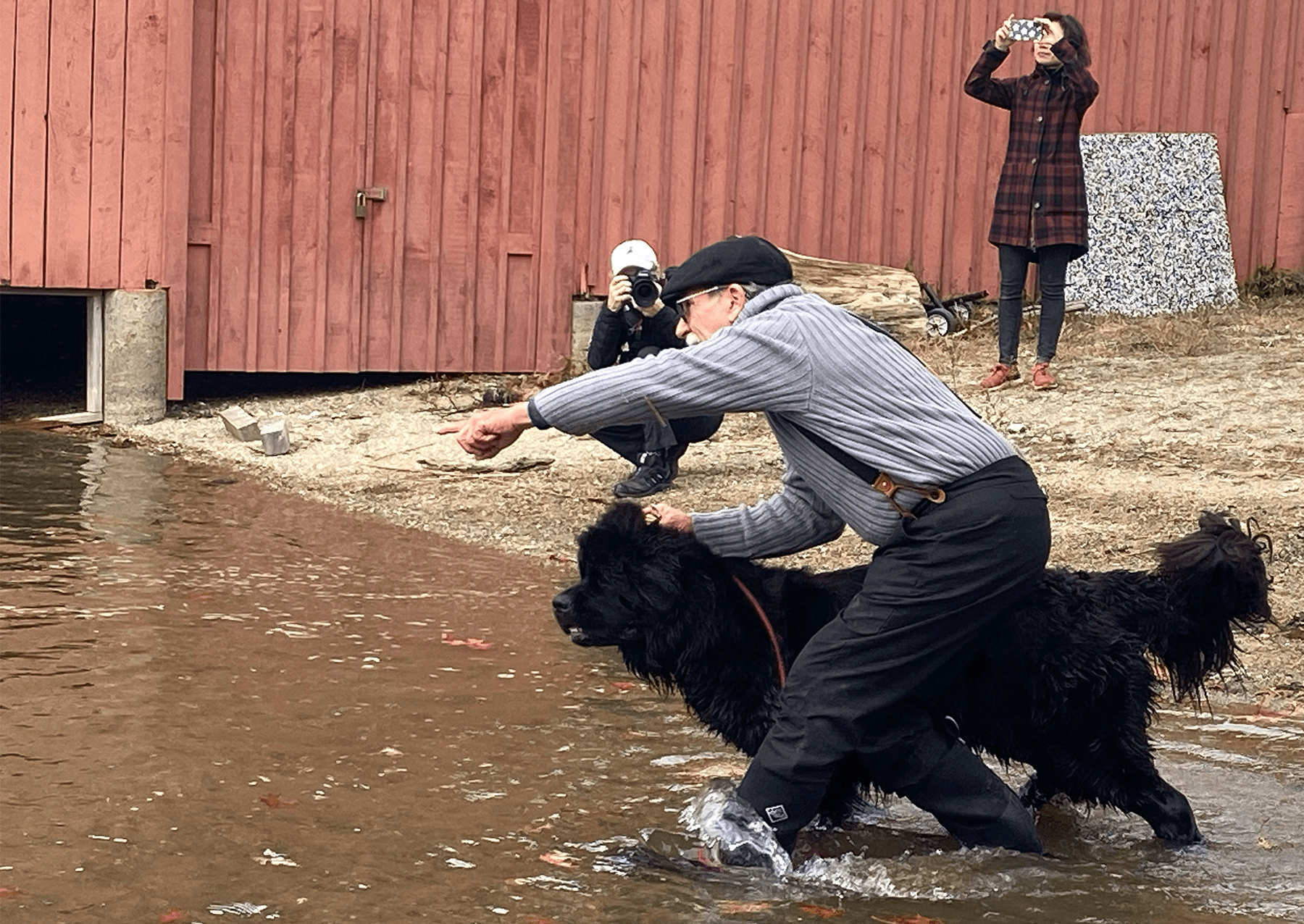 a man pointing out to the water with a black dog about to run in
